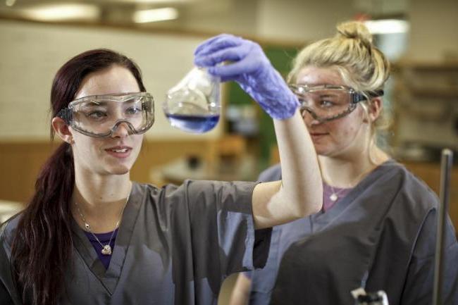 Two female students in a lab looking at a beaker filled with a purple liquid
